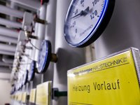 Das Bild zeigt eine Reihe von Messgeräten und Anzeigen, die mit Rohrleitungen verbunden sind. Ein gelbes Schild beschriftet mit "Heizung Vorlauf" hebt die Funktion dieser Systeme hervor. Die Messinstrumente zeigen Werte an, die für die Heizungsüberwachung relevant sind.