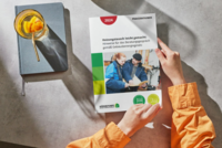 Auf dem Bild sind Hände zu sehen, die einen praktischen Ratgeber mit dem Titel "Heizungstausch leicht gemacht" halten. Der Ratgeber enthält Hinweise für Beratungsgespräche gemäß dem Gebäudeenergiegesetz. Im Hintergrund ist ein Notizbuch und ein Getränk mit einer Orangenscheibe sichtbar.