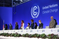 Eine Gruppe von Personen steht auf einer Bühne bei einer UN-Klimakonferenz. Sie tragen Masken und blicken in eine Richtung. Im Hintergrund ist das Logo der Vereinten Nationen und der Schriftzug "Climate Change" zu sehen. Die Atmosphäre wirkt formell und zusammenhängend.