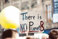 Ein Protest-Schild wird hochgehalten und trägt die Aufschrift „There is NO Planet B“. Es betont die Dringlichkeit des Umweltschutzes und die Notwendigkeit, unseren Planeten zu schützen. Hintergrund mit Menschen und unscharfen Gebäuden ist vorhanden, um die Atmosphäre einer Demonstration zu vermitteln.