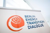 Ein Banner mit dem Text „Berlin Energy Transition Dialogue“ in blauer Schrift auf hellem Hintergrund. Links befindet sich ein oranges Symbol, das eine stilisierte Weltkugel darstellt.