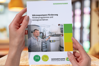 Eine Person hält ein Informationsblatt über Wärmepumpenförderung in den Händen. Das Blatt enthält Informationen zu Förderprogrammen und Antragsverfahren. Im Hintergrund ist eine moderne Heizungsanlage sichtbar.