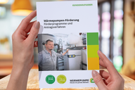 Eine Person hält ein Informationsblatt über Wärmepumpenförderung in den Händen. Das Blatt enthält Informationen zu Förderprogrammen und Antragsverfahren. Im Hintergrund ist eine moderne Heizungsanlage sichtbar.