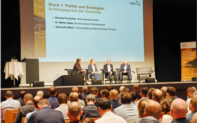 Eine Podiumsdiskussion mit vier Teilnehmern auf der Bühne, die über Politik und Strategien im Bereich Wärmepumpen sprechen. Im Hintergrund ist eine Präsentation an der Wand zu sehen, die den Titel „Block 1: Politik und Strategien“ trägt. Das Publikum sitzt vor der Bühne.
