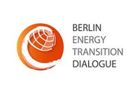 Logo des "Berlin Energy Transition Dialogue": Ein orangefarbenes Symbol mit stilisierter Weltkugel und geschwungenem Element, daneben der Schriftzug „Berlin Energy Transition Dialogue“. Das Logo repräsentiert den Dialog über den Übergang zu nachhaltiger Energie.