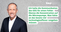 Ein lächelnder Mann in einem dunklen Anzug steht vor einer hellen Textur. Er äußert sich kritische zur Kommunikation des GEG und zur Konzentration auf Wärmepumpen. Er betont, dass das Gesetz technologieoffener gestaltet werden sollte.