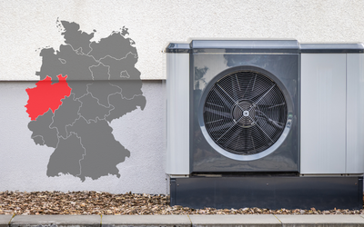 Eine Luftwärmepumpe steht an einer Wand, neben einer grauen Karte von Deutschland, die eine Region im Westen rot markiert. Das Bild zeigt die Kombination aus Heiz- und Kühltechnik und geografischer Lage.