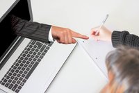 Ein Handarm in einem Anzug zeigt aus einem Laptopbildschirm auf eine Person, die an einem Notizblock mit einem Stift schreibt. Die Szene zeigt den Austausch von Informationen oder Ideen durch digitale Kommunikation.