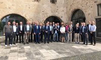 Eine Gruppe von etwa 30 Personen steht vor einem historischen Gebäude mit einem steinernen Fassadenhintergrund. Die Menschen tragen formelle Kleidung und lächeln. Es scheint sich um ein Treffen oder eine Konferenz zu handeln.