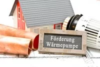 Das Bild zeigt einen Modellhaus, Kupferrohre, einen Heizkörper und ein Schild mit der Aufschrift „Förderung Wärmepumpe“. Diese Elemente stehen im Zusammenhang mit der Heiztechnik und möglichen Förderungen für Wärmepumpen im Bau- und Renovierungsbereich.