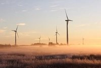 Eine Reihe von Windkraftanlagen steht in einer nebligen Landschaft während der Dämmerung. Sanfte Farben des Sonnenaufgangs umgeben die Windräder, die sich im leichten Wind drehen. Die Atmosphäre vermittelt ein Gefühl von Frieden und Natur.