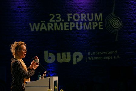 Eine Person steht an einem Podium und spricht auf dem 23. Forum Wärmepumpe. Sie hält ein Objekt in der Hand. Im Hintergrund sind das Logo des Bundesverbands Wärmepumpe e.V. und der Veranstaltungstitel sichtbar.