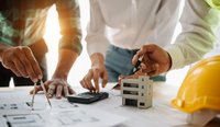 Drei Personen arbeiten an einem Tisch, auf dem Baupläne und ein Taschenrechner liegen. Sie nutzen einen Zirkel und einen Stift, um an den Plänen zu arbeiten. Vor ihnen steht ein Modell eines Gebäudes, sowie ein gelber Bauhelm, der das Bauprojekt symbolisiert.
