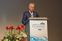 Ein Referent steht an einem Podium und spricht bei einem Forum zum Thema Wärmepumpen. Im Vordergrund sind Blumen zu sehen. Das Podium zeigt das Logo des Forums und Informationen zur Veranstaltung, die im November 2019 in Berlin stattfand.