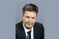 Ein Mann mit kurzem, grauem Haar trägt einen dunklen Anzug und eine hellere Krawatte. Er hat ein freundliches, aber ernstes Gesicht und blickt direkt in die Kamera. Der Hintergrund ist einfarbig und neutral gehalten.