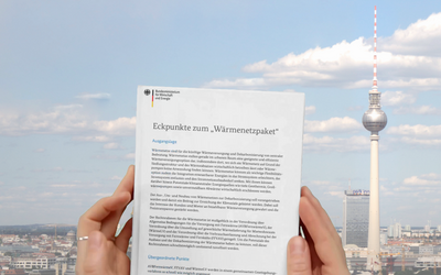 Eine Person hält ein Dokument mit dem Titel „Eckpunkte zum Wärmenetzpaket“ in den Händen. Im Hintergrund ist der Berliner Fernsehturm und ein klarer Himmel zu sehen.