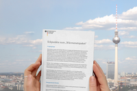 Eine Person hält ein Dokument mit dem Titel „Eckpunkte zum Wärmenetzpaket“ in den Händen. Im Hintergrund ist der Berliner Fernsehturm und ein klarer Himmel zu sehen.