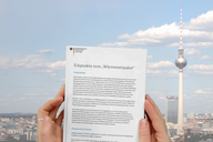 Eine Person hält ein Dokument mit dem Titel „Eckpunkte zum Wärmenetzpaket“ in den Händen. Im Hintergrund ist der Berliner Fernsehturm und ein klarer Himmel zu sehen.