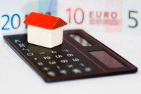 Ein kleines Holzhaus mit rotem Dach steht auf einer schwarzen Kreditkarte. Im Hintergrund sind schematische Euro-Scheine zu sehen. Das Bild symbolisiert finanzielle Themen, vermutlich im Zusammenhang mit Immobilien oder Finanzierungsfragen.