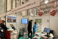 Ein Messestand des Bundesverbands Wärmepumpe (BWP) e.V. ist zu sehen. Es gibt Informationalmaterialien, einen Bildschirm mit Präsentationen und dekorative Elemente. Personen stehen in Gesprächsrunden, während Werbung für Wärmepumpen präsentiert wird. Ein positiver, einladender Eindruck wird vermittelt.