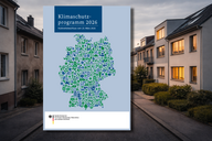 Titelbild des Klimaschutzprogramms 2026. Es zeigt eine grüne und blaue Illustration einer Karte Deutschlands, umgeben von Icons, die mit Umweltschutz und Nachhaltigkeit in Verbindung stehen. Der Hintergrund zeigt eine Wohnstraße mit modernen Gebäuden.