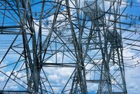 Ein Blick auf Hochspannungsmasten, die in den Himmel ragen. Die Struktur ist aus metallischen Elementen gefertigt, umgeben von einem blauen Himmel mit vereinzelten Wolken. Die Masten sind Teil des Stromnetzes und transportieren elektrische Energie.