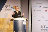 Eine Frau spricht vor einem Rednerpult bei einer Veranstaltung des Bundesverbands Erneuerbare Energien. Hinter ihr sind verschiedene Logos und das Veranstaltungslogo sichtbar. Sie gestikuliert und scheint eine wichtige Botschaft zu vermitteln, während das Publikum aufmerksam zuhört.