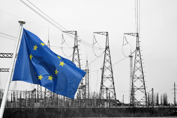 Die europäische Flagge weht im Vordergrund vor einer schwarz-weißen Landschaft mit Hochspannungsmasten im Hintergrund. Die Masten sind in verschiedenen Höhen und Formen dargestellt, was die industrielle Umgebung betont.