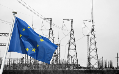 Die europäische Flagge weht im Vordergrund vor einer schwarz-weißen Landschaft mit Hochspannungsmasten im Hintergrund. Die Masten sind in verschiedenen Höhen und Formen dargestellt, was die industrielle Umgebung betont.