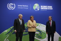 Drei Politiker stehen auf einer Bühne bei einer Klimakonferenz. Im Hintergrund ist ein grafisches Element mit einer Erdkugel und Aufschriften zur UN-Klimakonferenz 2021 zu sehen. Die Atmosphäre ist freundlich, alle Beteiligten lächeln und scheinen sich zu unterhalten.