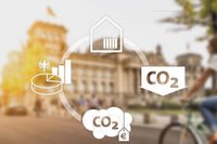 Illustration, die ein Diagramm zur CO2-Reduktion zeigt. Es umfasst Symbole wie ein Haus, ein Kreisdiagramm und CO2-Emissionen. Im Hintergrund ist ein unscharfes Gebäude zu sehen, das auf politische oder wirtschaftliche Themen hindeutet.