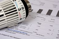 Ein Heizkörperthermostat liegt auf einem Rechnungsdokument. Auf dem Dokument sind verschiedene Zahlen und Beträge aufgeführt, die sich auf den Energieverbrauch und die Kosten beziehen. Der Fokus liegt auf der Abrechnung für den Stromverbrauch.