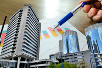 Eine Hand hält einen blauen Stift über Diagramme und Grafiken, während im Hintergrund moderne Bürogebäude und ein hohes Hochhaus zu sehen sind. Die Grafiken zeigen farbige Balken, die wirtschaftliche Daten darstellen.