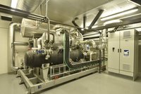 Eine industrielle Maschine steht in einem Technikraum. Sie ist mit vielen Rohren und einem Bedienfeld ausgestattet. Die Maschine wird zur Kühlung oder Energieerzeugung verwendet und ist auf einem stabilen Gestell montiert, um Funktionalität und Sicherheit zu gewährleisten.