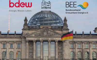 Das Bild zeigt das Reichstagsgebäude in Berlin. Im Vordergrund sind die Logos von bdew und BEE, zwei Organisationen, die sich mit Energie beschäftigt. Die deutsche Flagge weht sichtbar. Das Bild vermittelt ein Gefühl der Energie- und Wasserversorgung in Deutschland.