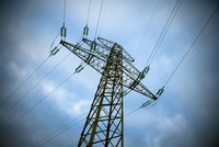 Eine Stromleitung, bestehend aus einem hohen, gelben Mast, der oben mit einer Metallstruktur und Isolatoren ausgestattet ist. Die Leitungen erstrecken sich horizontal und sind vor einem wolkigen, blauen Himmel sichtbar.