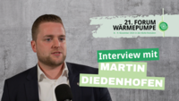 Bildbeschreibung: Ein junger Mann mit kurzen, blonden Haaren spricht in ein Interview. Er trägt ein dunkelblaues Jackett über einem weißen Hemd. Im Hintergrund ist eine graue Wand. Hinweis auf das 21. Forum Wärmepumpe, das am 8. und 9. November 2023 stattfindet.