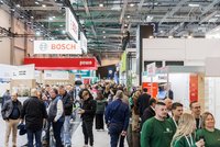 Eine belebte Messehalle mit vielen Besuchern, die zwischen den Ausstellungsständen umhergehen. Im Hintergrund sind Banner von verschiedenen Marken, darunter Bosch und pewo, sichtbar. Die Atmosphäre ist geschäftig und bunt.