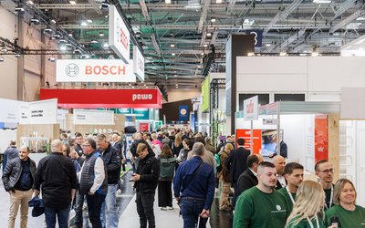 Eine belebte Messehalle mit vielen Besuchern, die zwischen den Ausstellungsständen umhergehen. Im Hintergrund sind Banner von verschiedenen Marken, darunter Bosch und pewo, sichtbar. Die Atmosphäre ist geschäftig und bunt.