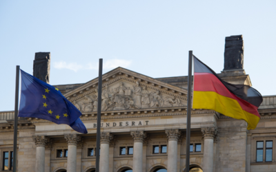 Das Bild zeigt die Flaggen der Europäischen Union und Deutschlands vor dem Gebäude des Bundesrats. Über dem Eingangsbereich ist der Schriftzug „Bundesrat“ sichtbar. Der Himmel ist klar und blau.