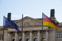 Das Bild zeigt die Flaggen der Europäischen Union und Deutschlands vor dem Gebäude des Bundesrats. Über dem Eingangsbereich ist der Schriftzug „Bundesrat“ sichtbar. Der Himmel ist klar und blau.