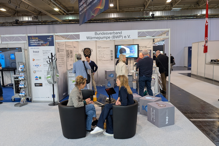 Ein Messestand des Bundesverbands Wärmepumpe (BWP) e.V. mit mehreren Besuchern. Zwei Personen sitzen in schwarzen Sesseln und sprechen Laptop. Im Hintergrund sind weitere Aussteller und Informationsmaterialien sichtbar.