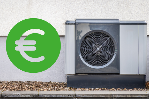Eine Wärmepumpe steht an einer Wand, daneben ist ein großes grünes Euro-Symbol. Die Pumpe hat ein graues Gehäuse und einen sichtbaren Lüfter. Der Boden ist mit kleinen Steinen bedeckt.