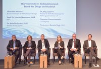 Ein Podiumsgespräch zum Thema "Wärmewende im Gebäudebestand: Stand der Dinge und Ausblick". Auf der Bühne sitzen sechs Fachleute, darunter Vertreter aus der Politik und der Industrie. Der Fokus liegt auf den Herausforderungen und Perspektiven der Wärmewende. Moderation durch Kerstin Vogt.