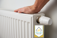 Eine Hand dreht an einem Heizkörperthermostat. Der Heizkörper ist weiß und an einer Wand angebracht. In der Ecke befindet sich ein Logo mit dem Text „#WocheDerWärme“.