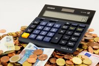 Ein schwarzer Taschenrechner steht auf einem Haufen Münzen und Geldscheinen. Die sichtbaren Geldscheine sind in Euro. Der Bildschirm des Rechners zeigt die Zahl 19 an. Der Rechner hat Tasten für Euro- und Steuerberechnungen.