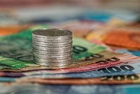 Einstapel von Münzen in der Mitte, umgeben von verschiedenen Geldscheinen in unterschiedlichen Farben. Der Fokus liegt auf der Stapelung der Münzen, während die Geldscheine unscharf im Hintergrund liegen.