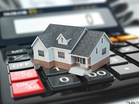 Ein kleines Modellhaus steht auf einem Taschenrechner. Die Tasten des Rechners sind sichtbar, um das Thema Finanzen und Immobilien zu verdeutlichen. Die Szene symbolisiert die Berechnung von Hypotheken oder Immobilienwerten.