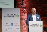 Ein Mann in Anzug steht an einem Rednerpult und spricht beim 22. Forum Wärmepumpe in Berlin. Im Hintergrund ist eine Mauer aus Ziegelsteinen zu sehen. Auf dem Pult befindet sich ein Schild mit den Details zu dem Event, das am 27. und 28. November 2024 stattfindet.