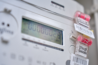 Ein digitaler Stromzähler zeigt den aktuellen Verbrauch in kWh an. Auf dem Zähler sind mehrere farbige Clips mit Barcodes angebracht. Der Bildschirm ist hell und gut lesbar, mit einer Anzeige von "000000.02 kWh".